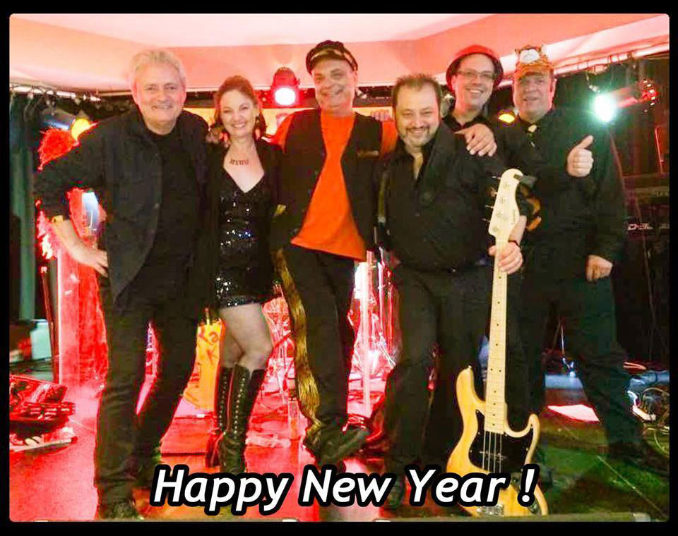 Six band members posed on a red-lit stage in party hats, one holding a bass guitar, with a Happy New Year caption across the photo.